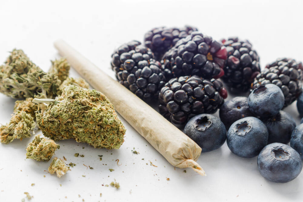 cannabis buds next to a joint and blackberries and blueberries