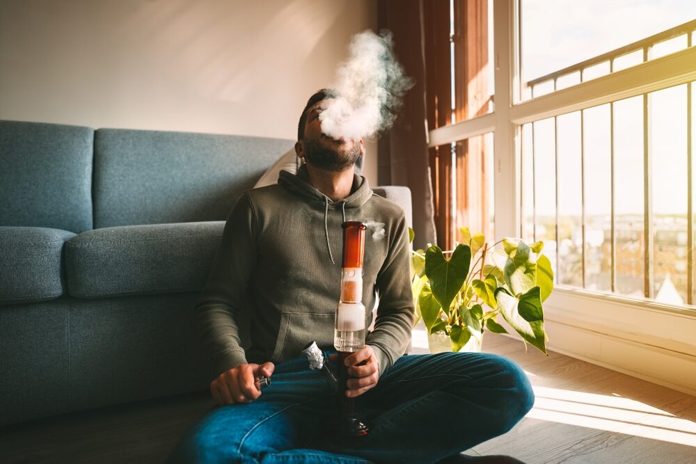 man smoking cannabis bong in room