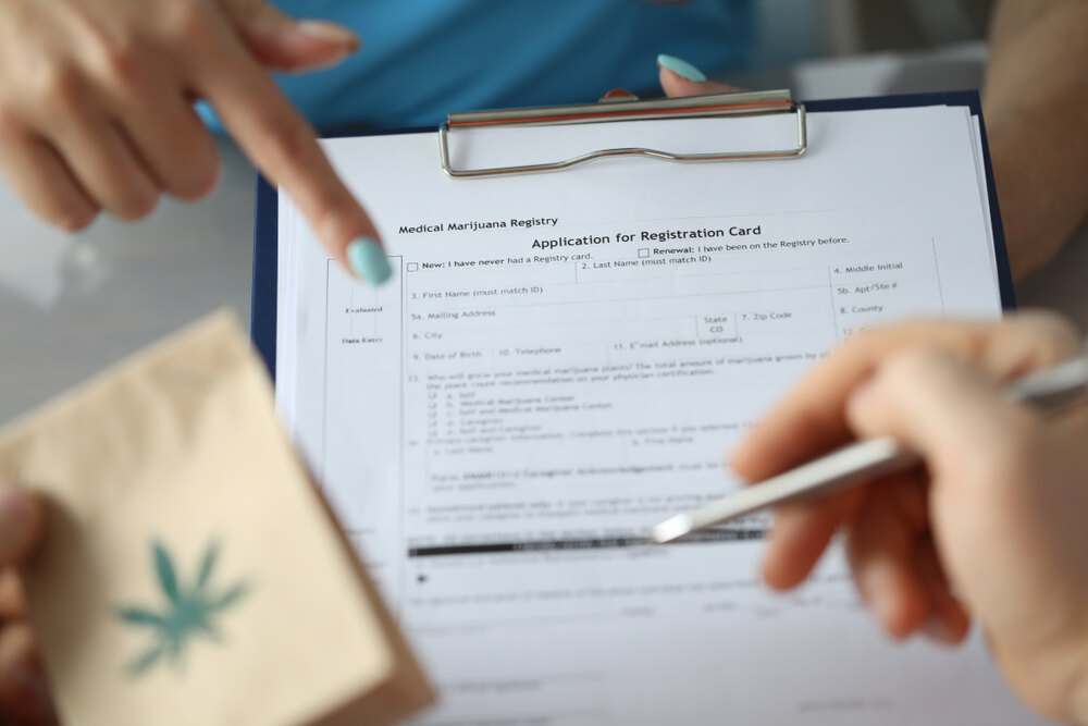a hand pointing to a cannabis registration form for medical card with marijuana bag
